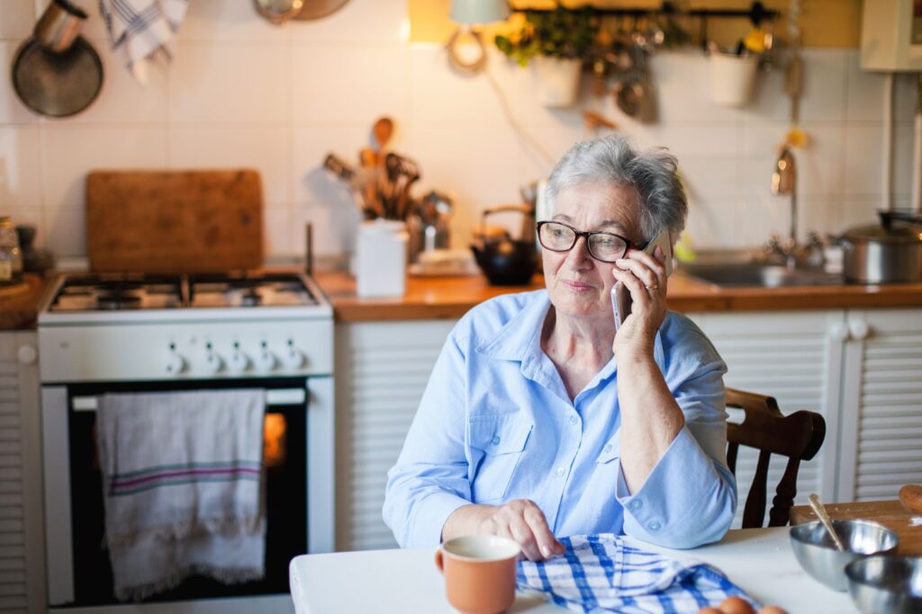 Senior woman talking on mobile phone at home kitchen